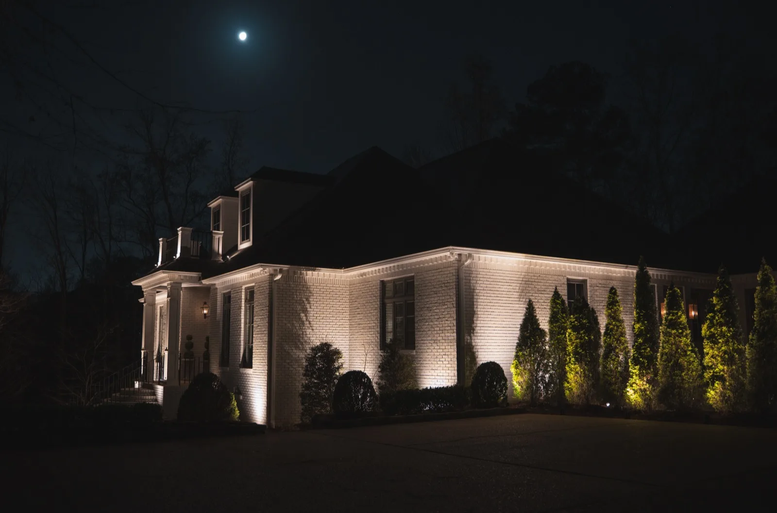 White brick home up-lit at night under a full moon